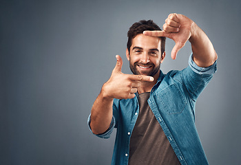 Image showing Frame, hands and portrait of man in studio on gray background with happiness, confident and smile. Finger border, mockup and male person face with hand sign for picture, photography and perspective