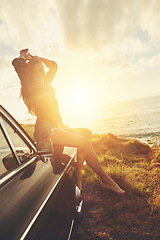 Image showing Road trip, portrait and sunset with a woman at the coast, sitting on her car bonnet during travel for freedom or escape. Nature, lens flare and water with a young female tourist traveling in summer