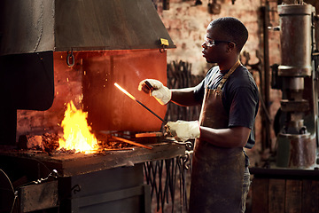 Image showing Blacksmith, fire and a black man melting metal in a workshop for manufacturing or industrial design. Factory, welding or industry with a male designer in metalwork using a hot flame to melt material