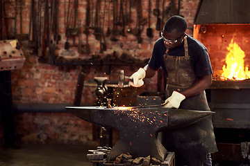 Image showing Blacksmith, worker and metal forge in workshop and manual industry working on hot steel with hammer, sparks or fire. Black man, welding or iron tools manufacturing or expert, trade and dark workspace