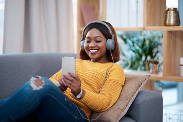 Image showing Relax, phone and music with a black woman on a sofa in the living room of her home streaming audio through headphones. Mobile, freedom and time off with a happy young female listening to the radio