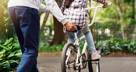 Image showing Father teaching his child to ride a bicycle on a path in an outdoor green community park. Love, bonding and closeup of a man helping his girl kid on a bike in garden for fun, exercise and development