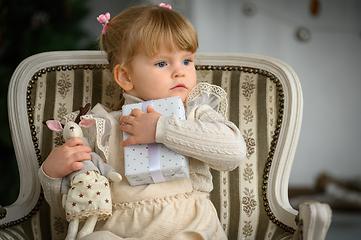 Image showing Little blond girl sits in a chair in front of Christmas tree