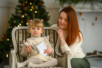 Image showing Little blond girl in a chair and her mother together in front of Christmas tree