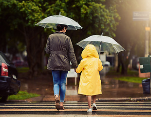 Image showing Back, raincoat or umbrella with a mother and daughter walking across a street in the city during winter. Autumn, crosswalk or park with a woman and female child holding hands while crossing a road