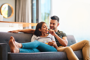 Image showing Love, happy couple on sofa and eating chips in living room of their home. Caring or bonding together, relaxing or comfortable and happy married people on couch watching television for quality time.