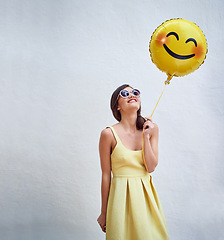 Image showing Woman, balloon and happy by wall in with emoji, smile and face for fashion sunglasses at party, event or celebration. Gen z and girl and excited with icon, space and yellow dress to celebrate spring