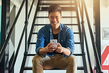 Image showing Asian man, texting and office stairs with phone, smile and communication on social network app. Young japanese businessman, web design startup and relax on steps in workplace for chat with smartphone