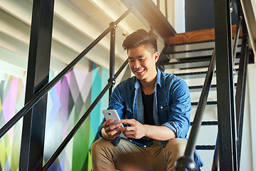 Image showing Asian man, texting and office stairs with smartphone, smile and communication on social network app. Young japanese creative, web design startup and relax on steps in workplace for chat with phone