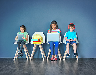 Image showing Chairs, children, and technology for learning and education while online for research on internet. Kids or students against a blue mockup wall with laptop, tablet and video on phone in a waiting room