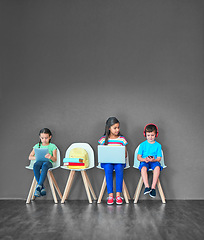 Image showing Children, chair and technology for learning and education while online for research on internet. Kids or students against a grey mockup wall with laptop, tablet and phone in a waiting room with space