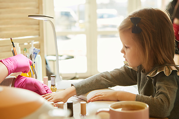 Image showing Little girl in nail salon receiving manicure by beautician. Little girl getting manicure at beauty salon.