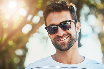 Image showing Sunglasses, casual and portrait of a happy man in an outdoor park while on a vacation, adventure or holiday. Smile, confidence and young male person with eyewear standing in a garden on weekend trip.