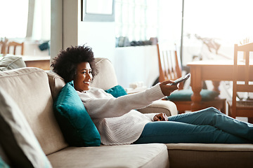 Image showing Black woman, watching tv and relax on couch with remote, home and happiness for me time, comedy or show. African girl, television and happy for movie, video or search on living room sofa in apartment