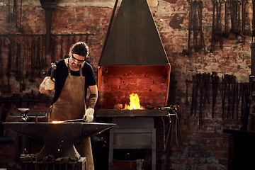 Image showing Blacksmith, forge and man in metal workshop and manual working on hot steel with hammer, sparks and fire. Master, welding job or iron tools manufacturing and expert, trade and dark workspace