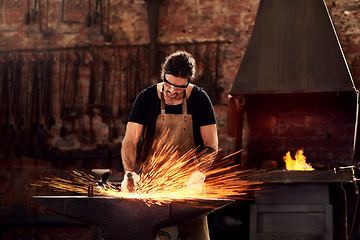 Image showing Blacksmith, man and metal workshop and sparks, manual forge working on hot steel with hammer, and fire. Worker, person welding or iron tools manufacturing and expert, trade and dark workspace