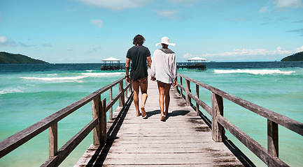 Image showing Travel, freedom and rear view of couple at beach walking, holding hands and relax on ocean jetty with blue sky background. Summer, holiday and behind man with woman at sea, traveling or Bali romance