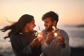 Image showing Love, beach and couple with sparklers for celebration, party and quality time on romantic date. Nature, sunset and happy man and woman with fireworks for honeymoon on holiday, weekend and vacation