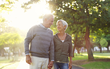 Image showing Senior couple, walking and holding hands outdoor at a park with love, care and support. A elderly man and woman in nature for a walk, quality time and communication for healthy marriage or retirement