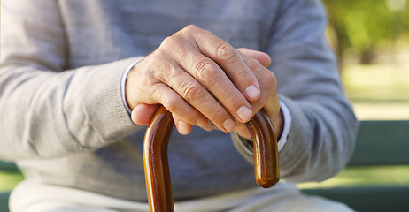 Image showing Closeup of senior hands on a walking cane for help, assistance or healthcare in outdoor park. Nature, retirement home and zoom of elderly male person with disability sitting in garden with wood stick