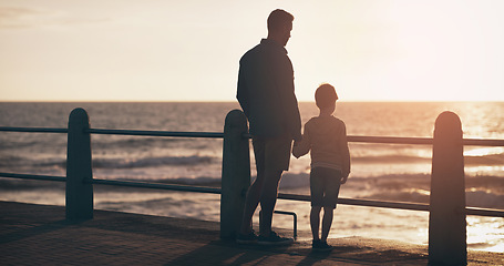 Image showing Silhouette, sunset and a father holding hands with his son on the promenade at the beach while walking together. View, family or kids and a man bonding with his young male child outdoor in nature