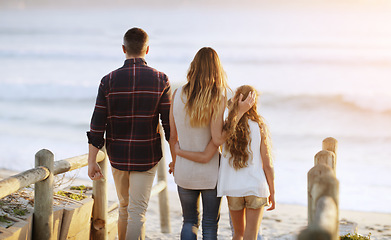 Image showing Family, back and walking together at beach with love, care and bonding on vacation with sunset, waves and kid. Father, mother and daughter with embrace, walk and ocean with dusk sunshine on holiday