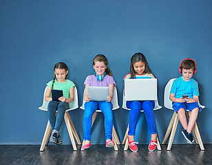 Image showing Children with a laptop, tablet and phone for learning and education while online for research on internet. Kids or students against a blue mockup wall with technology on chairs in a waiting room