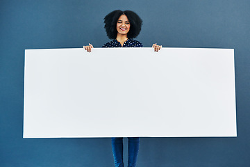 Image showing Space, poster and portrait of happy woman in studio with banner for news, social media or advertising on blue background. Paper, billboard and female smile with mockup, sticker and branding promotion