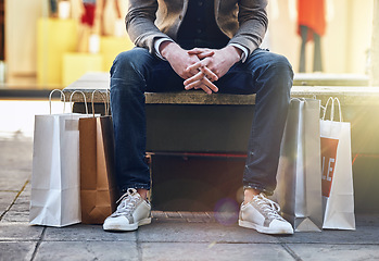 Image showing City, man sitting and sale with shopping bags on floor, sidewalk or street with sneakers, relax or waiting for taxi. Guy, retail and fashion on bench in metro cbd with discount, promotion or clothes