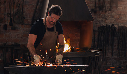 Image showing Hammer, anvil and fire with a man working in a forge for metal work manufacturing or production. Industry, welding and trade with a male blacksmith at work in a factory, plant or industrial workshop