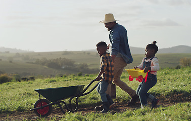 Image showing Man, son and daughter working on a farm with a wheel barrow for agriculture in the countryside. Family, farming and children work in the outdoor of a rural environment with joy and fun for learning.