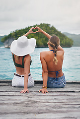 Image showing Women, lake and friends outdoor with heart hand sign on deck to relax with peace, water and love. Back of female people with hands, icon and freedom on vacation, holiday or summer adventure in nature