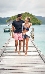 Image showing Happy couple, tropical and ocean boardwalk with walking, hug and outdoor in summer sunshine for holiday. Man, woman and walk together by sea with love, happiness and care with travel for vacation