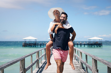 Image showing Happy couple, vacation and walking on ocean boardwalk for piggy back, freedom and travel. A man and woman playing and laughing on tropical walk to relax on holiday, nature adventure or date at sea