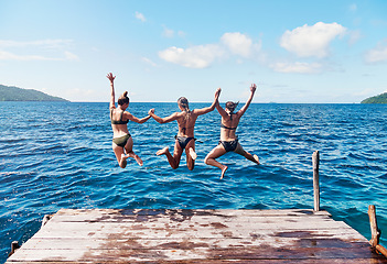 Image showing Water, back of people jumping off a pier holding hands and into the ocean together in blue sky. Summer vacation or holiday break, freedom or travel and young group of friends diving into the lake