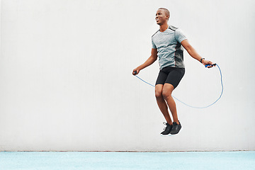 Image showing Jump, rope and space with black man skipping in stadium for sports, workout and cardio. Performance, health and body with male athlete training on track for strong, mockup and exercise by wall