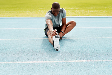 Image showing Athlete man, sitting and track for stretching legs to start training, exercise or running for fitness outdoor. African runner, warm up muscle or body for workout at stadium for race, contest or sport