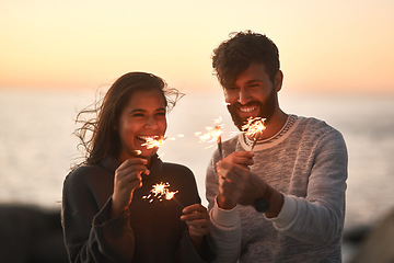 Image showing Sunset, beach and couple with fireworks for celebration, party and sparks on romantic date. Nature, love and happy man and woman with sparklers for honeymoon on holiday, weekend and vacation