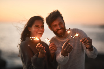 Image showing Happy, beach and couple with sparklers for celebration and party with sparks on romantic date. Love, sunset and excited man and woman with fireworks for honeymoon on holiday, weekend and vacation