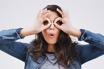 Image showing Portrait, funny face and finger glasses with a woman in studio on a gray background looking silly or goofy. Comedy, comic and playing with a crazy young female person joking indoor for fun or humor