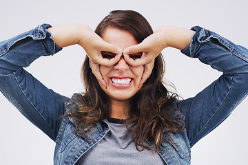 Image showing Portrait, funny face and finger glasses with a woman in studio on a white background looking silly or goofy. Comedy, comic and smile with a crazy young female person joking indoor for fun or humor