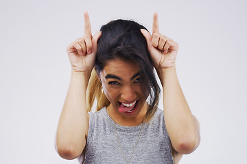 Image showing Portrait, funny face and devil horns with a woman in studio on a gray background looking silly or goofy. Comedy, comic and playing with a crazy young female person joking for carefree fun or humor