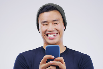 Image showing Phone, laugh and Asian man online in studio with smile for social media, internet humor and funny chat. Communication, gray background and male person on smartphone for website, mobile app and meme