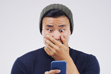 Image showing Asian man, surprise and phone in shock for winning, prize or good news against a white studio background. Shocked or surprised male person reading on mobile smartphone in wow for lottery competition