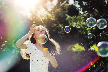 Image showing Girl child, bubbles and backyard garden with mockup space in summer sunshine by trees for playing game. Female kid, blowing bubble and outdoor with soap, games and rainbow in nature, park and mock up