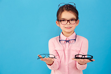 Image showing Portrait, mockup and choice by kid with glasses for vision or eye care promotion isolated in a blue studio background. Smile, decision and girl child with sale, discount and deal option for eyewear