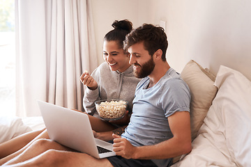 Image showing Watching movie, popcorn and couple in bed with laptop for streaming, food and internet. Subscription, happy and comic with man and woman at home for social media, funny and free time on weekend