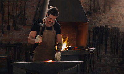 Image showing Hammer, anvil and fire with a man working in a foundry for metal work manufacturing or production. Industry, welding and trade with a young male blacksmith in a workshop, plant or industrial forge