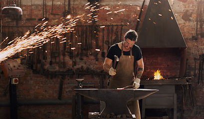 Image showing Hammer, anvil and fire with a man working in a factory for metal work manufacturing or production. Industry, welding and trade with a male blacksmith at work in a forge, plant or industrial workshop