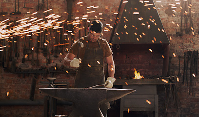 Image showing Hammer, anvil and fire with a man in a forge workshop for metal work manufacturing or production. Industry, welding and trade with a male blacksmith at work in a factory, plant or industrial foundry